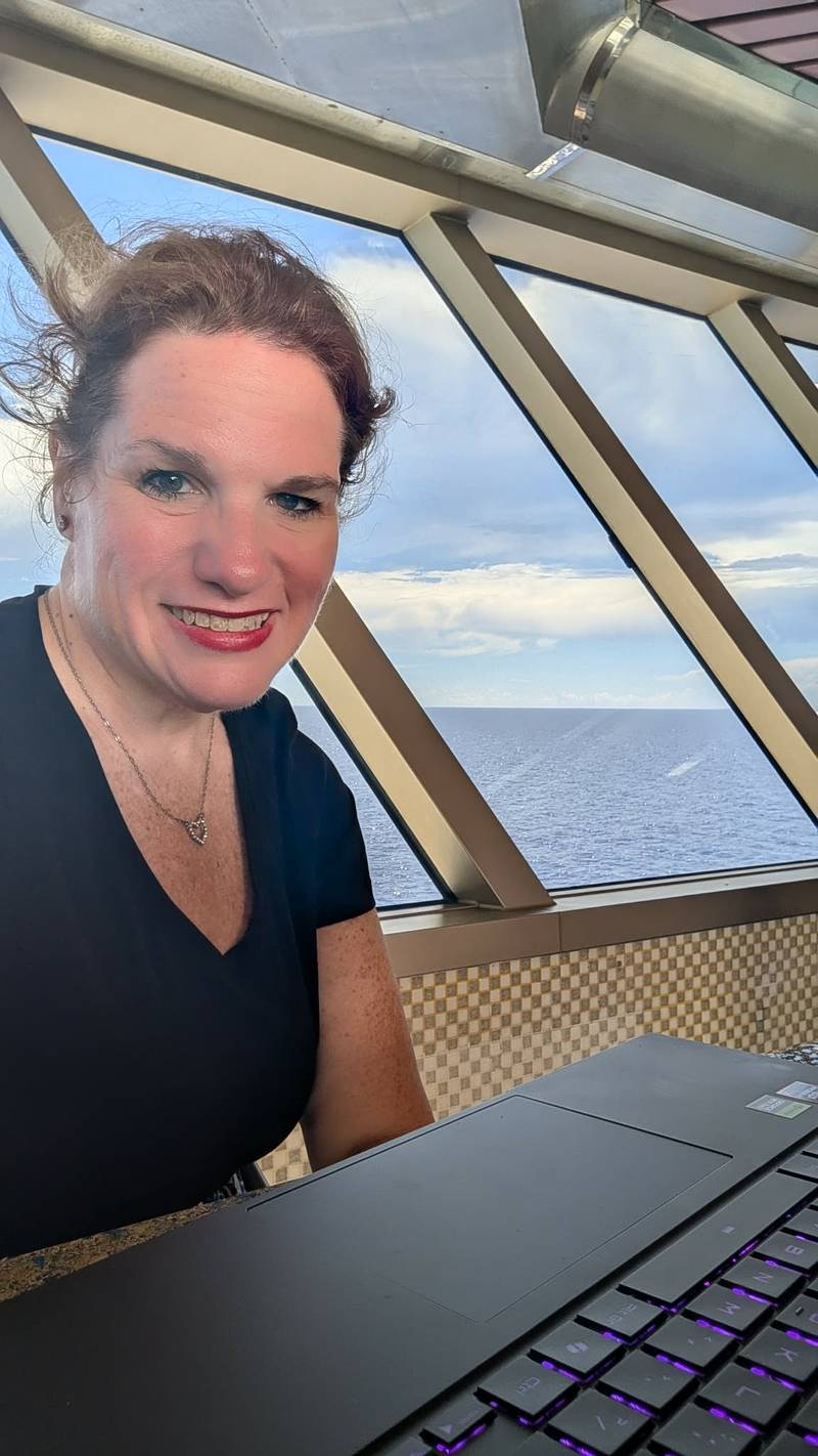 Kellie working on her laptop by a cruise ship window at sea
